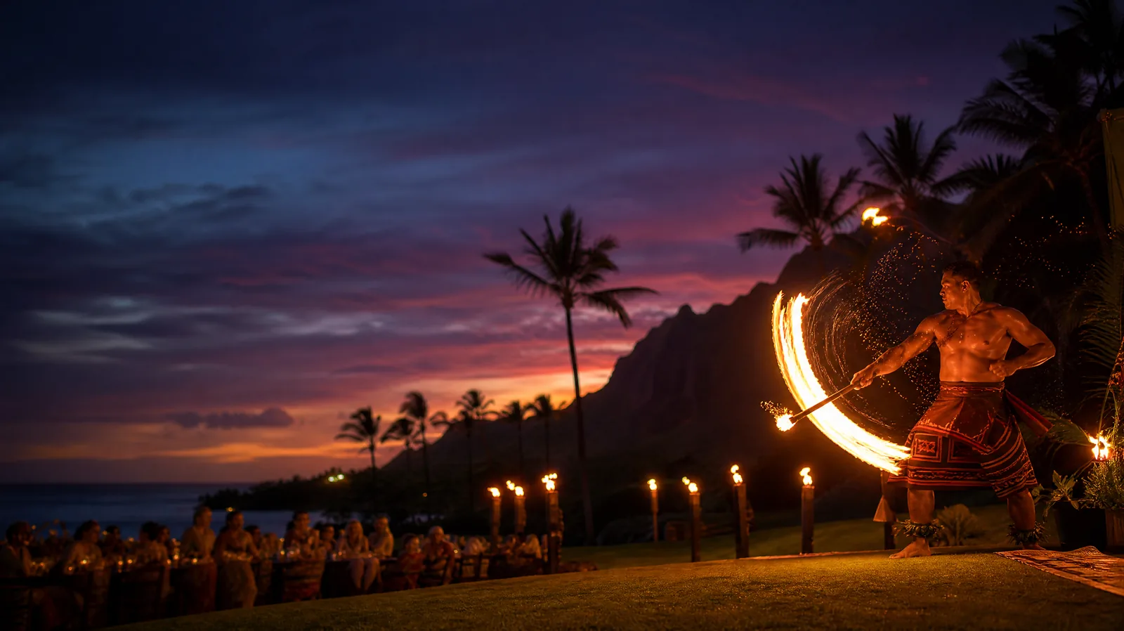 Fire knife dancer at a torch-lit Kauai luau at sunset